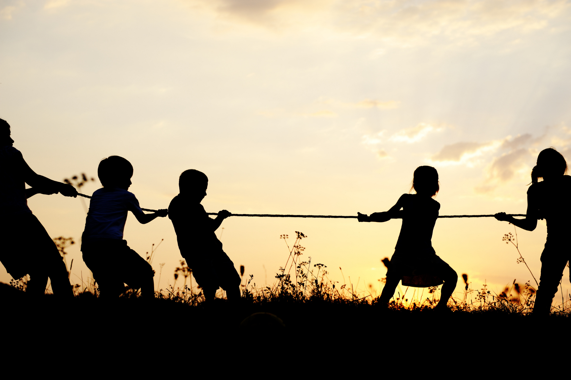 Silhouettes of campers pulling a rope together at sunset